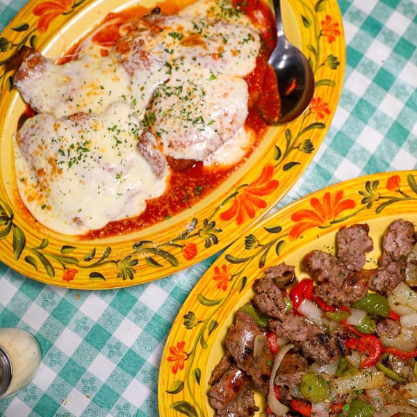 Two yellow plates of Italian dishes, one with chicken parmesan and the other with sausage, peppers, and onions.