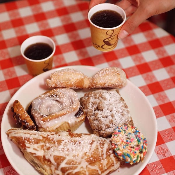 A plate of assorted pastries and two small cups of coffee on a red and white checkered tablecloth.