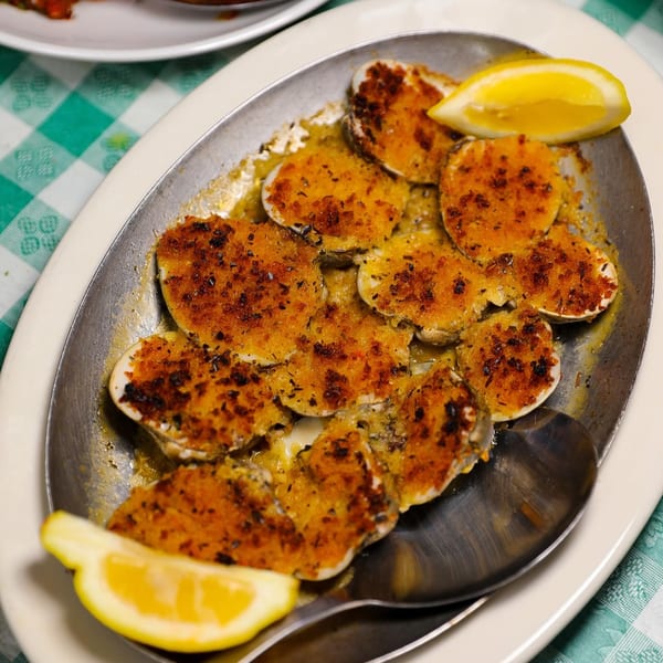 Baked clams with breadcrumbs and herbs, garnished with lemon wedges, served on a metal platter.