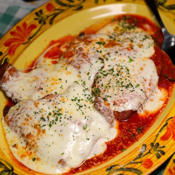 Chicken Parmesan with melted mozzarella and marinara sauce on a decorative yellow plate.