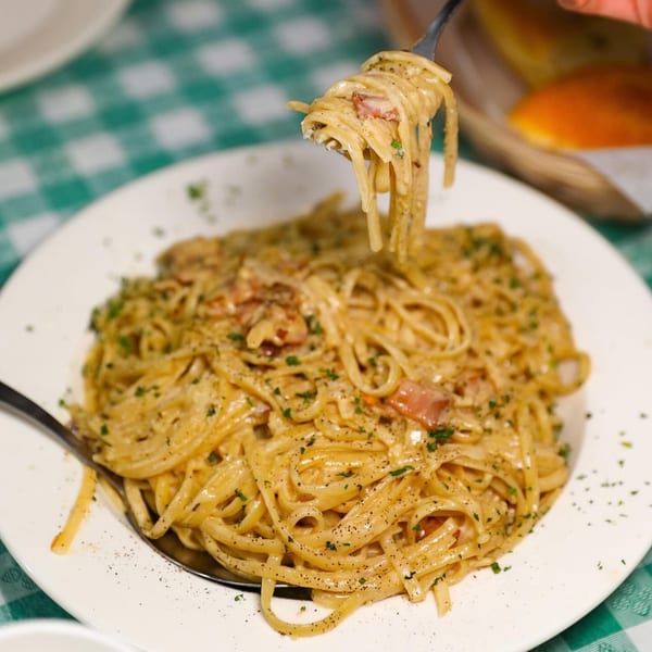 Creamy pasta with bacon and herbs on a white plate, with a fork lifting some noodles.
