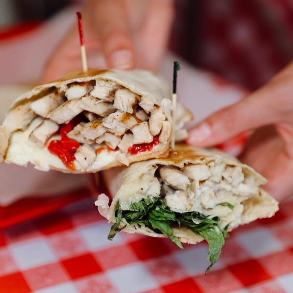 Two hands hold two halves of a chicken wrap, one with red peppers, the other with greens.