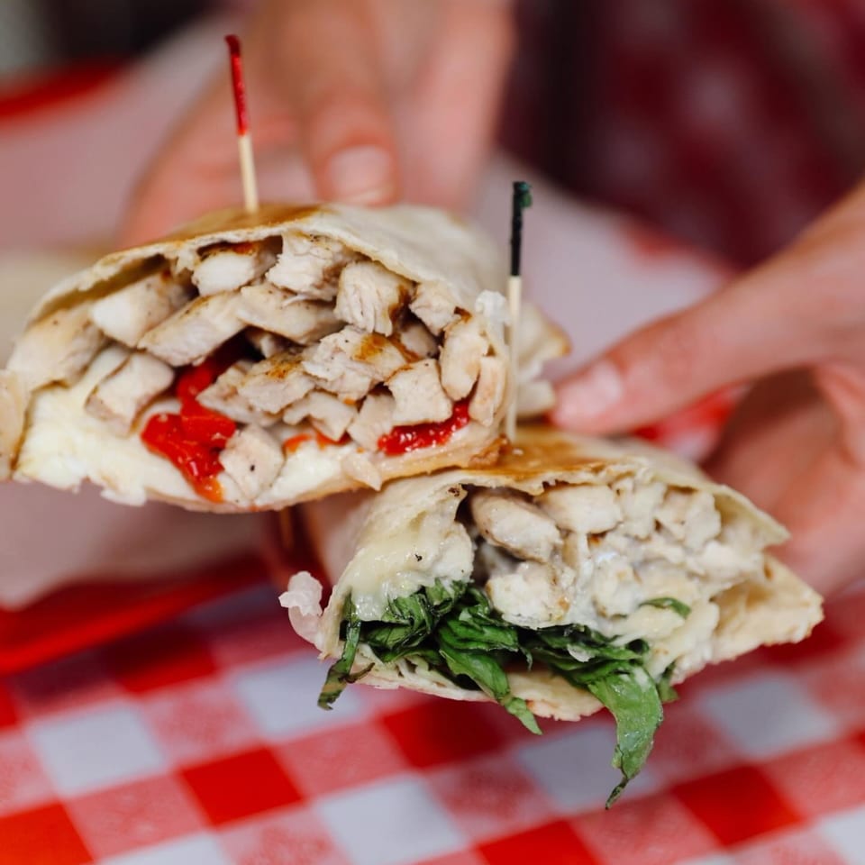Two hands hold two halves of a chicken wrap, one with red peppers, the other with greens.